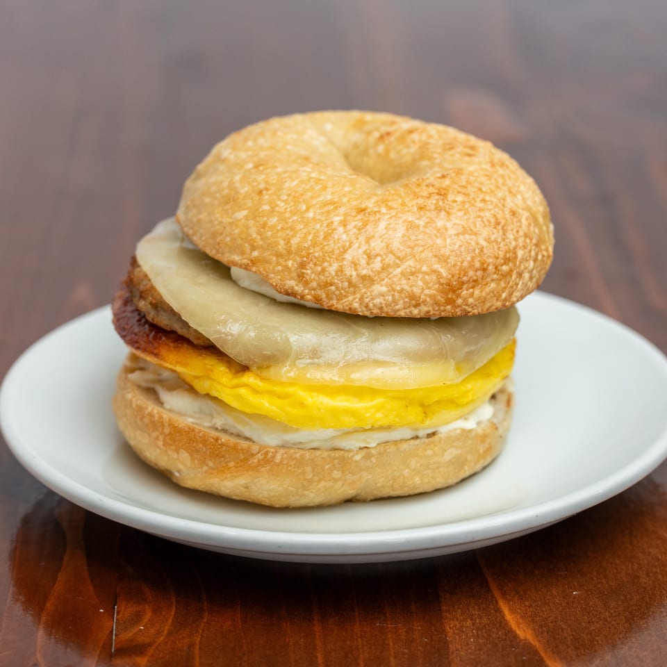 Breakfast sandwich with egg, melted cheese, and grilled onions on a toasted bagel, served on a white plate.