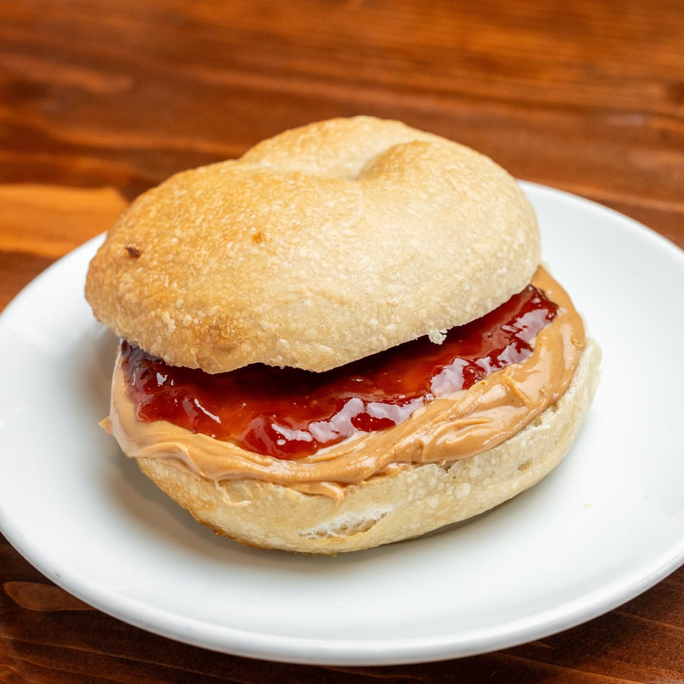 Peanut butter and jelly sandwich on a white plate atop a wooden table.