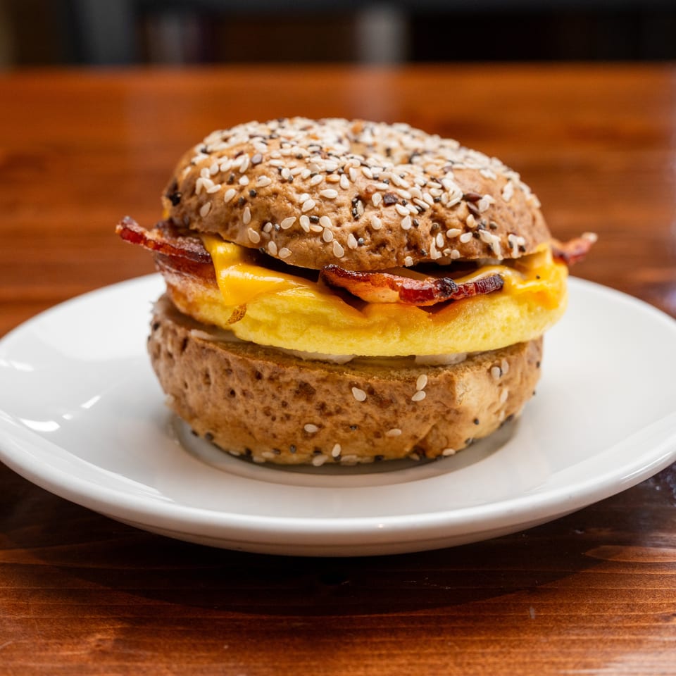 Bacon cheeseburger on a seeded bun, served on a white plate atop a wooden table.