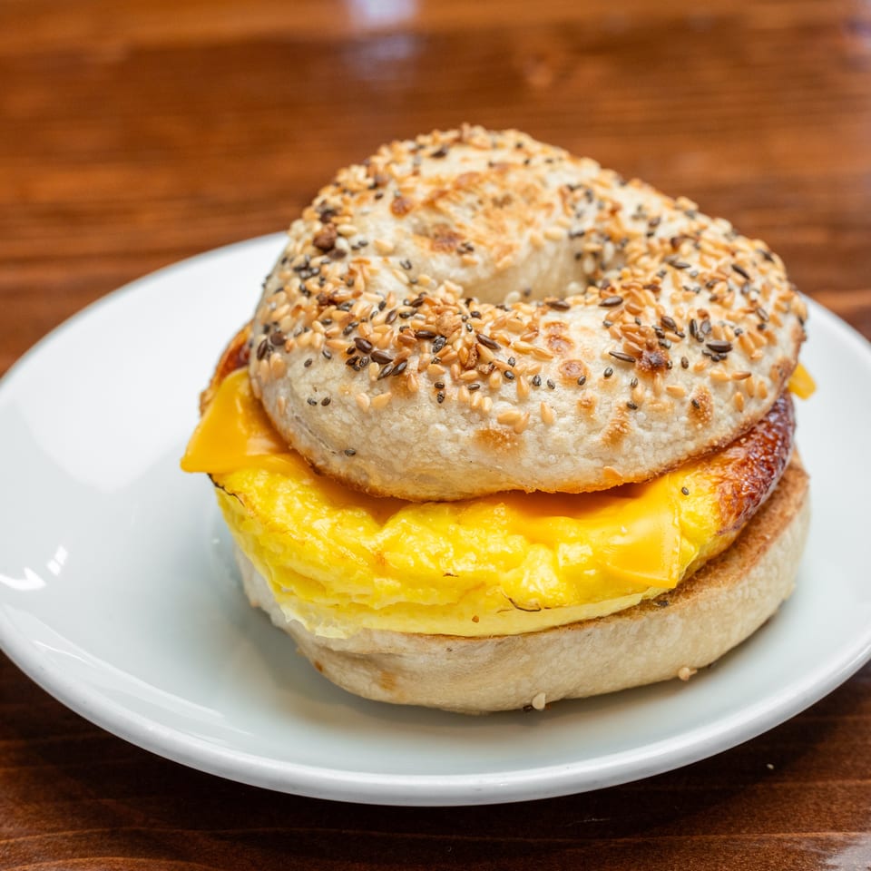 Sesame-seeded breakfast sandwich with fluffy scrambled eggs and melted cheese on a white plate.