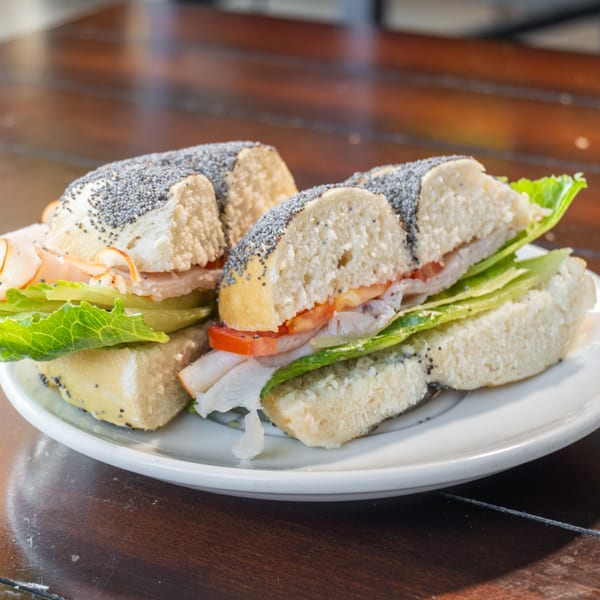 Assorted poppy-seed sandwiches with sliced turkey, lettuce, tomato, and cucumber served on a white plate.