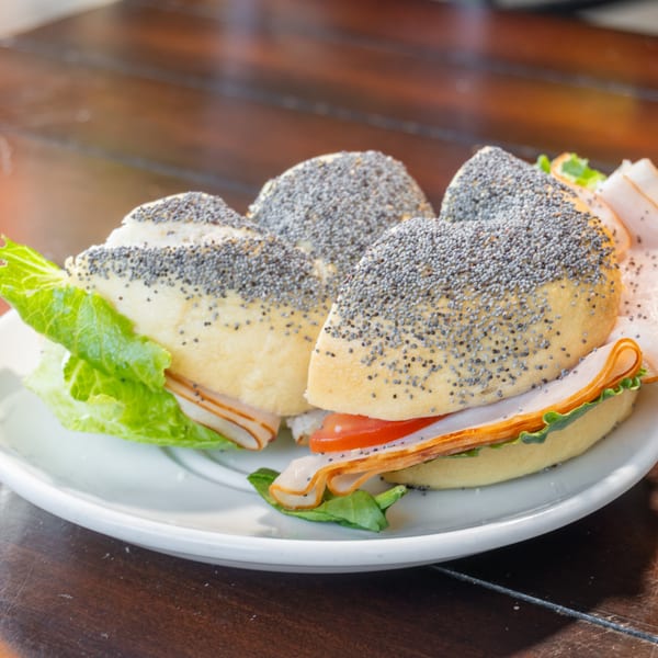 Plate of poppy-seed sandwiches filled with sliced turkey, lettuce, tomato, and cheese on a wooden table.