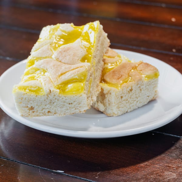 Slices of white cake topped with glossy yellow glaze on a white plate atop a dark wooden table.