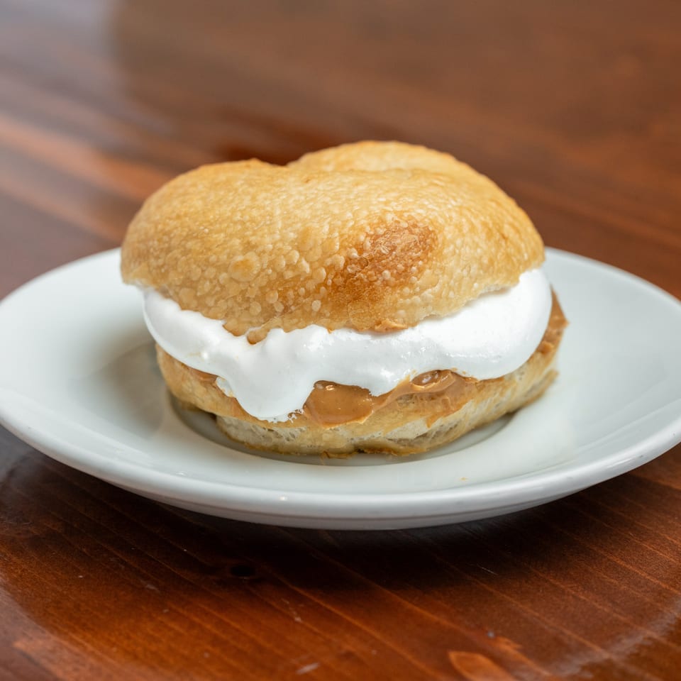 Golden pastry filled with thick white cream and caramel sauce, served on a white plate atop a wooden table.
