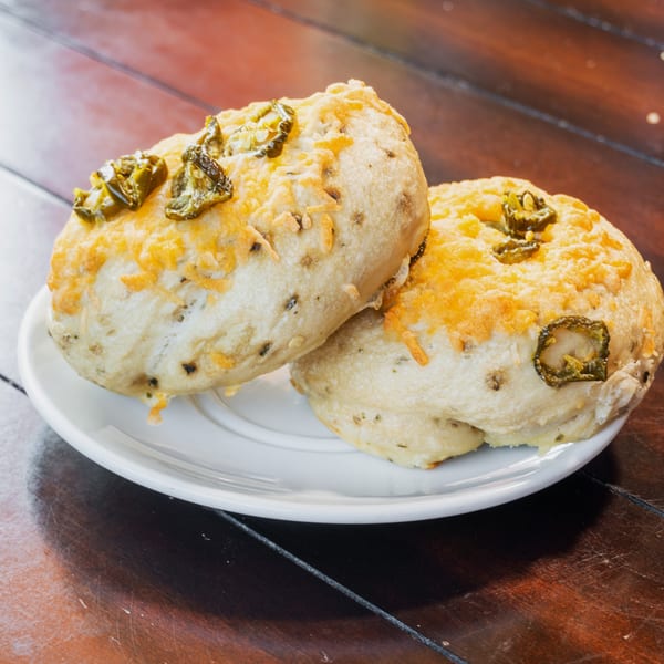 Three cheesy jalapeño biscuits arranged on a white plate atop a dark wooden table.