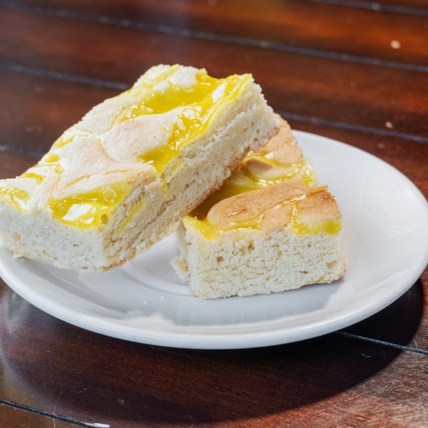 Slices of white cake drizzled with bright yellow glaze sit on a white plate atop a dark wooden table.