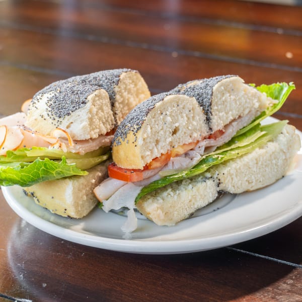 Plate of poppy-seed sandwiches filled with sliced turkey, tomato, cucumber, and lettuce on a wooden table.