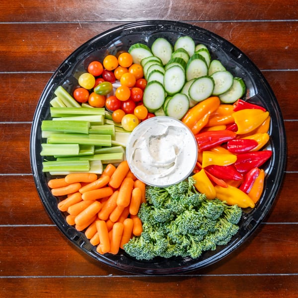 Vegetable platter with carrots, celery, broccoli, cucumbers, tomatoes, peppers, and ranch dip on a wooden table.