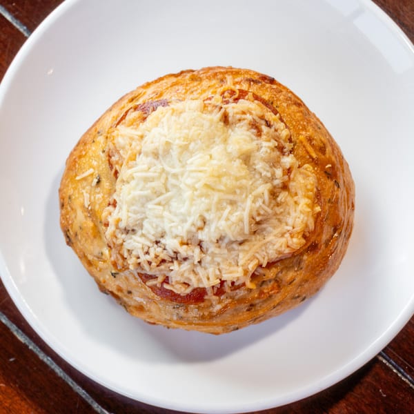 Golden-brown round savory pastry topped with melted shredded cheese, served on a white plate atop a wooden table.