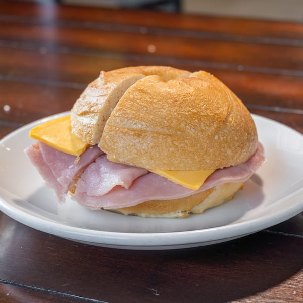 Ham and cheese sandwich on a crusty roll, served on a white plate atop a wooden table.