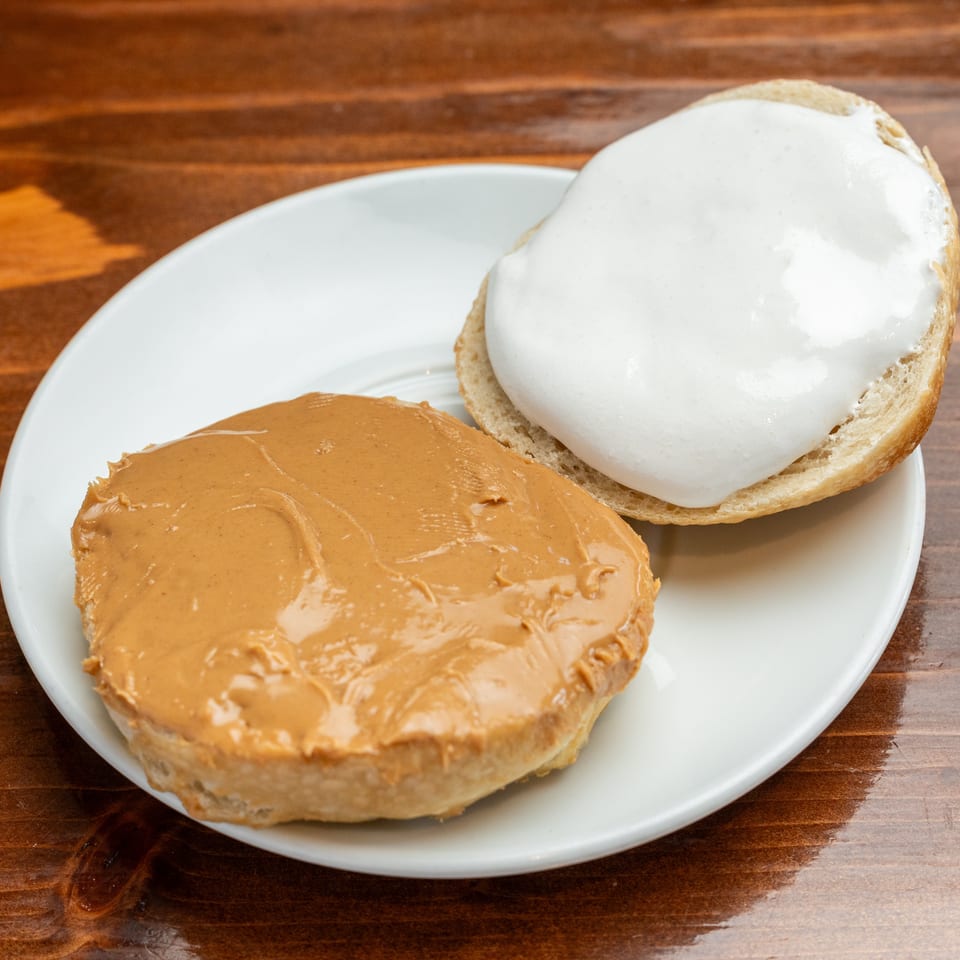 Two bagel halves on a white plate, one spread with peanut butter and the other topped with white cream cheese.