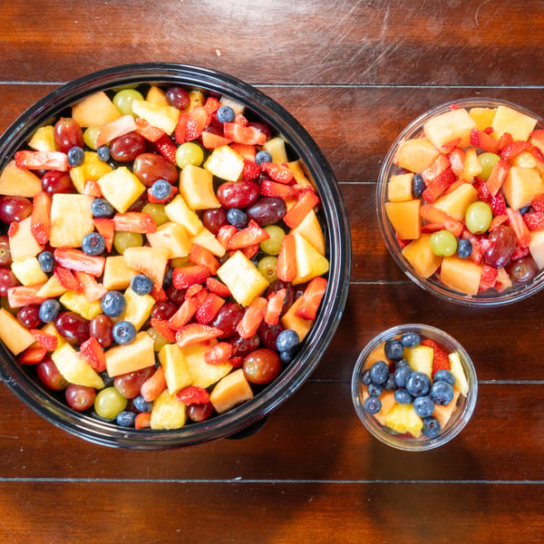 Bowls of colorful fresh fruit salad with strawberries, blueberries, grapes, pineapple, and melon on a wooden table.